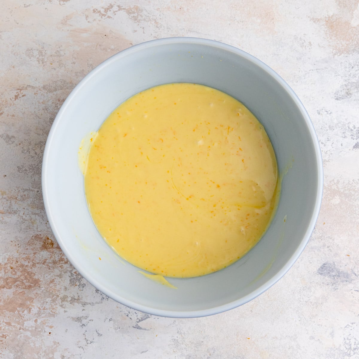 Orange muffin batter without the flavor in the white ceramic bowl. The batter is a light orange color.