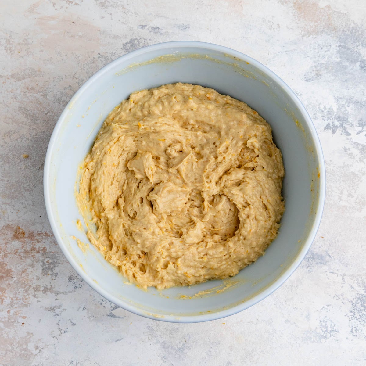The orange muffin batter in a white ceramic bowl. The batter is a light orange color