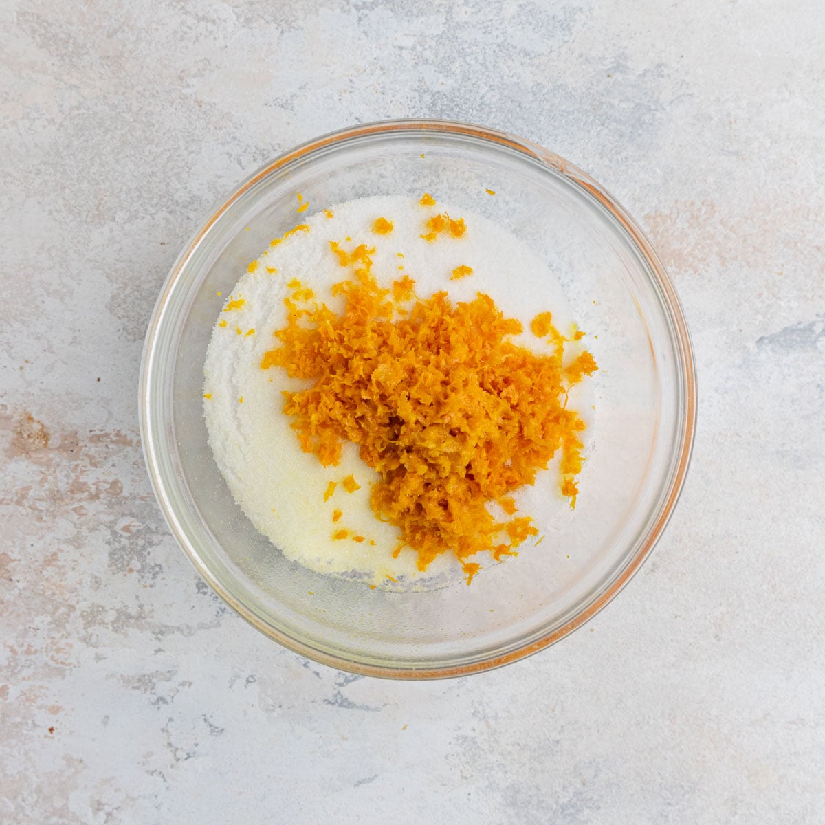 Fresh orange zest on top of granulated sugar in a small bowl