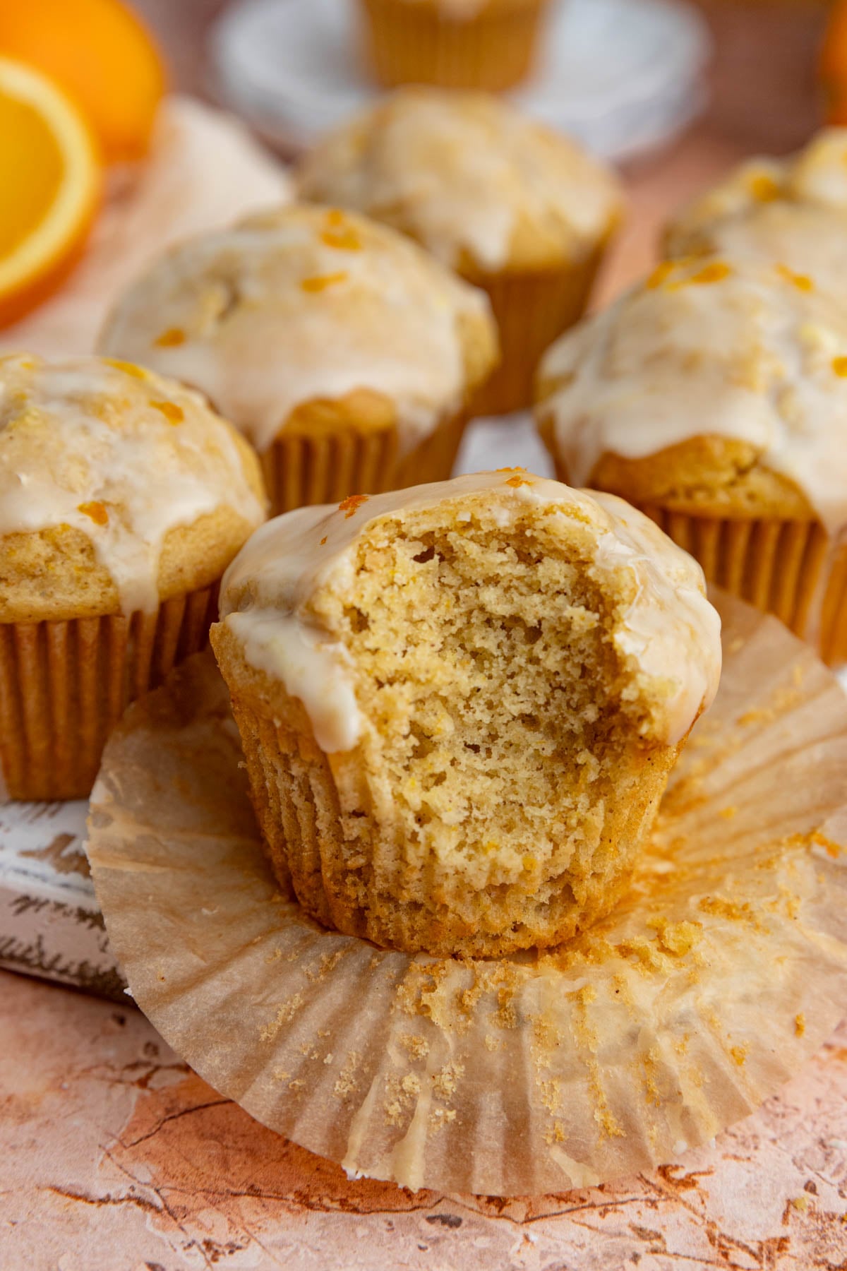 An orange muffin with a bite taken out of it. There are 5 other muffins near and behind that muffin.