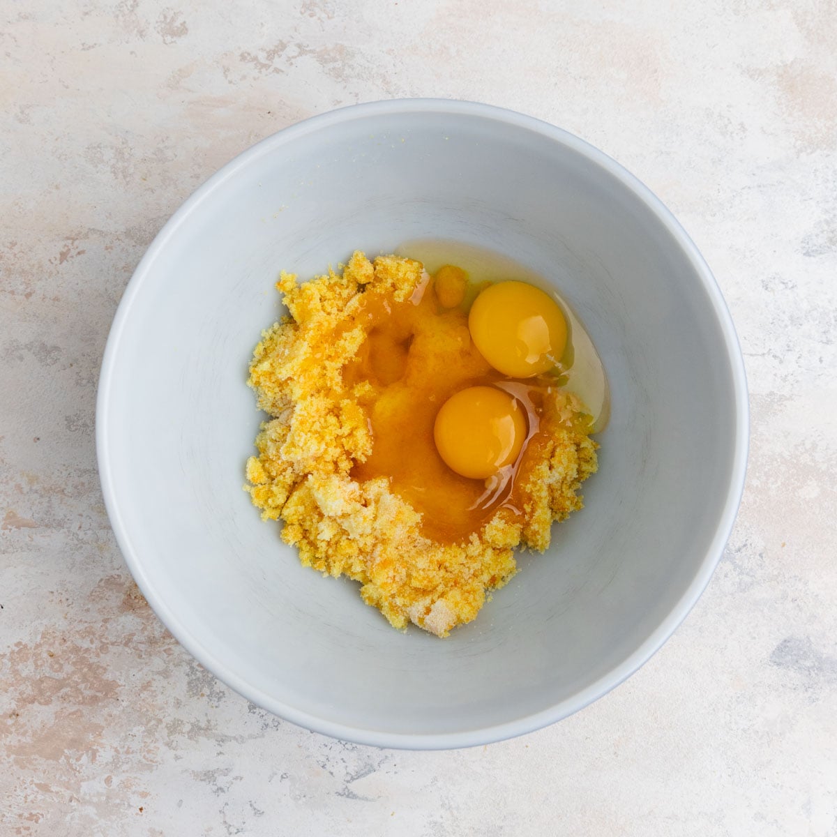 Two eggs added to the orange zest-sugar mixture in a ceramic mixing bowl
