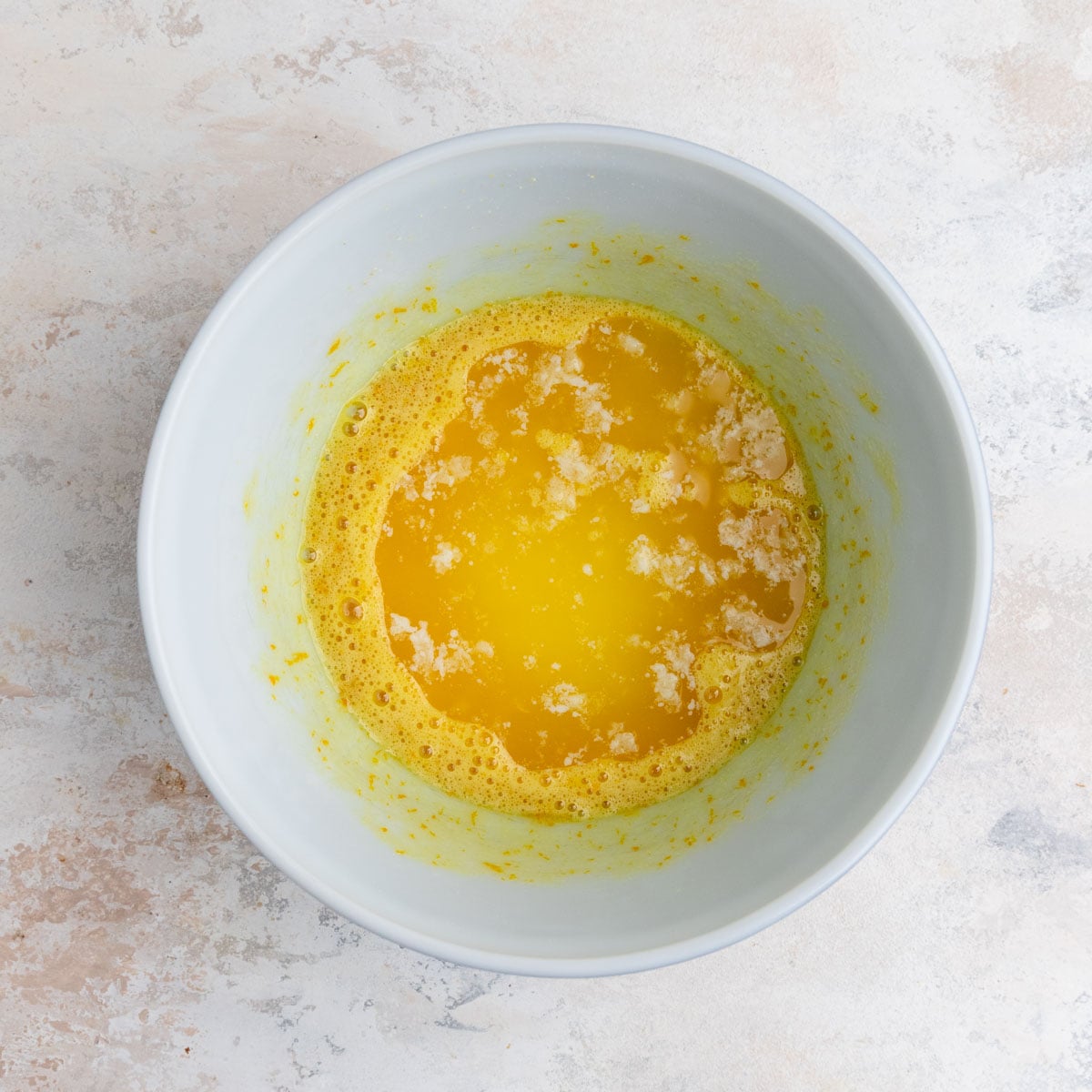 Melted butter added to the orange muffin batter in a white ceramic mixing bowl