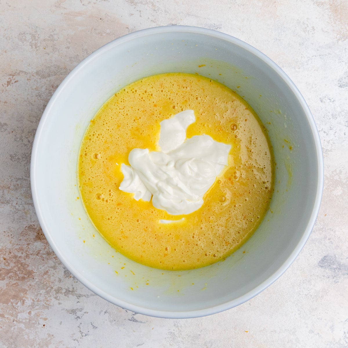 Sour cream added to the muffin batter in a white ceramic bowl