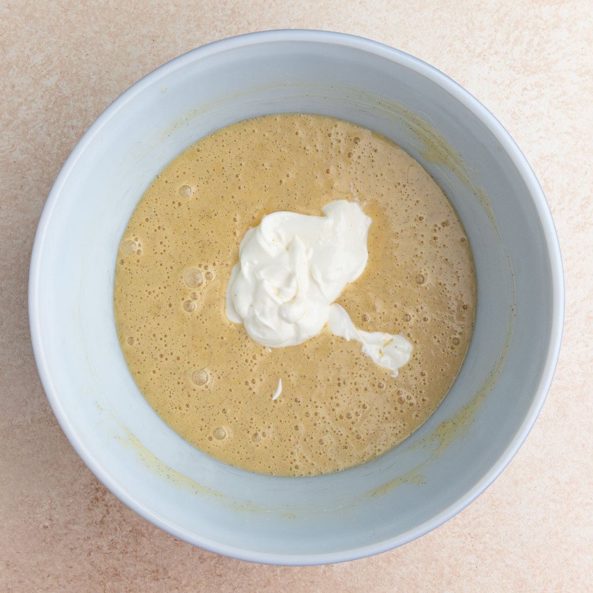 Sour cream added to the vanilla muffin batter in a large bowl