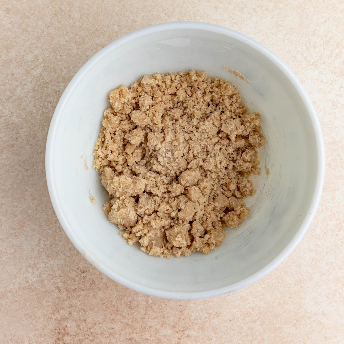 The cinnamon crumble in a white ceramic bowl.  The crumble is a combination of small and large pieces