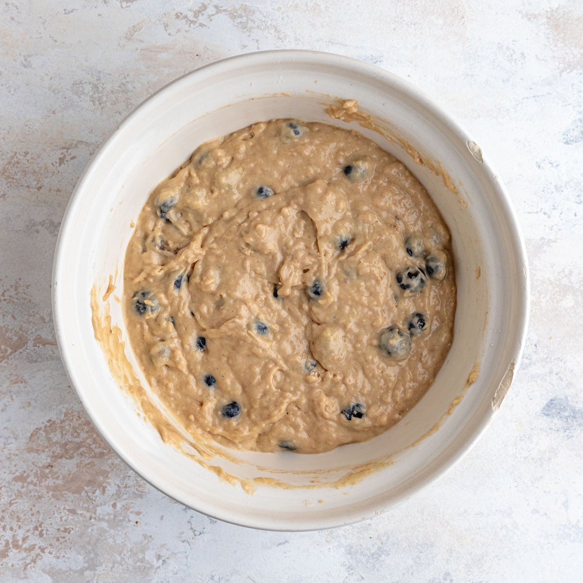 The muffin batter in a large ceramic bowl, with the blueberries mixed in