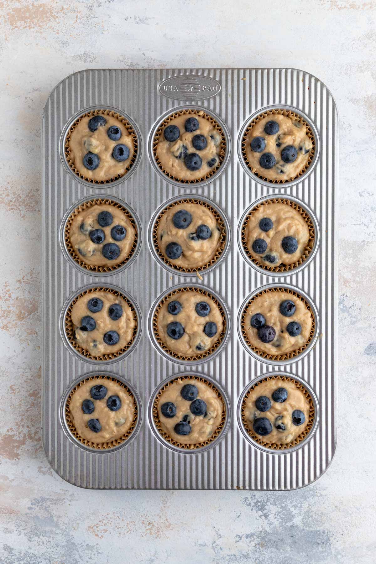 The muffin batter spooned into a 12 cup muffin tin.  Three to four blueberries dot the top of each muffin