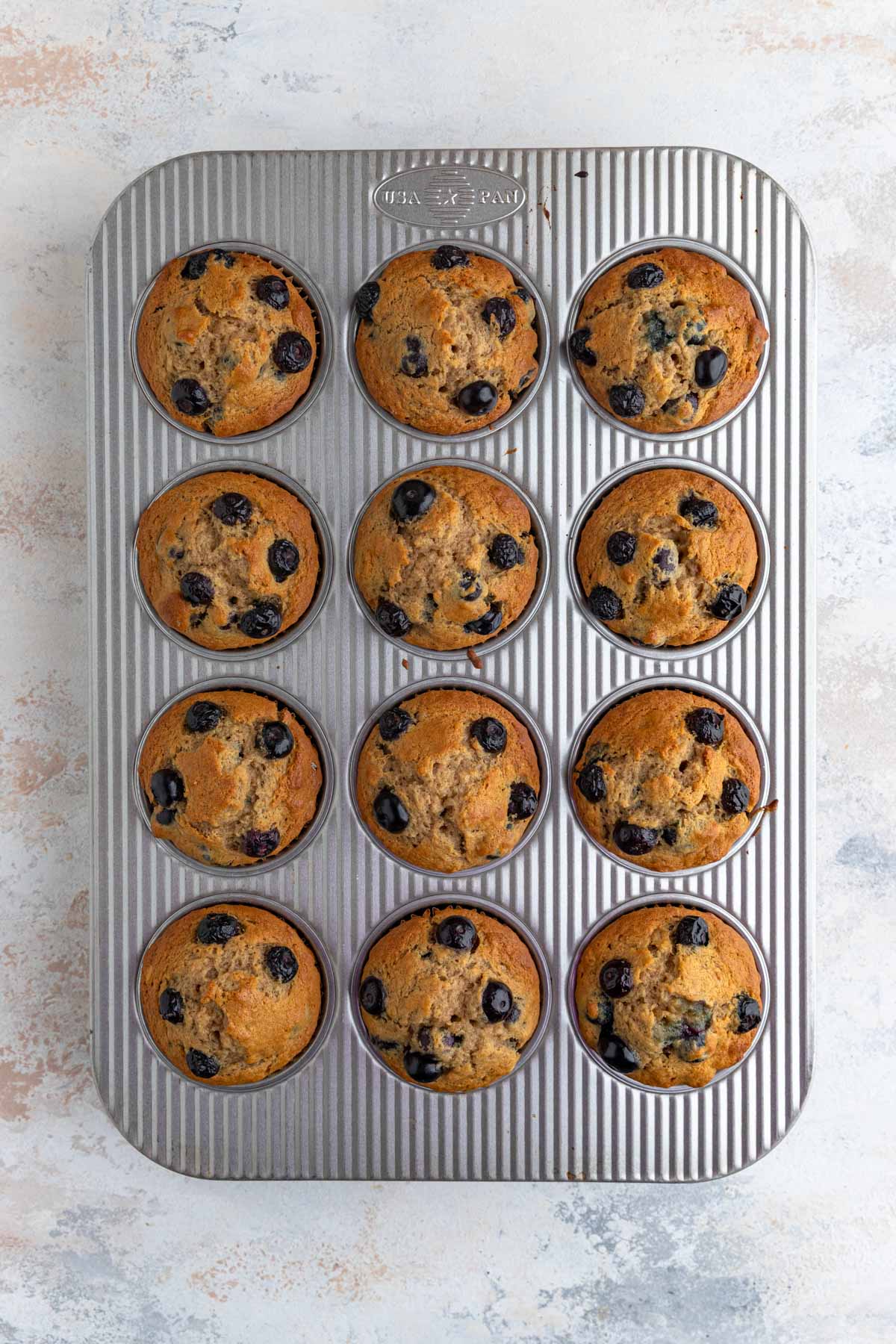 Twelve baked blueberry banana muffins in a 12-cup muffin tin