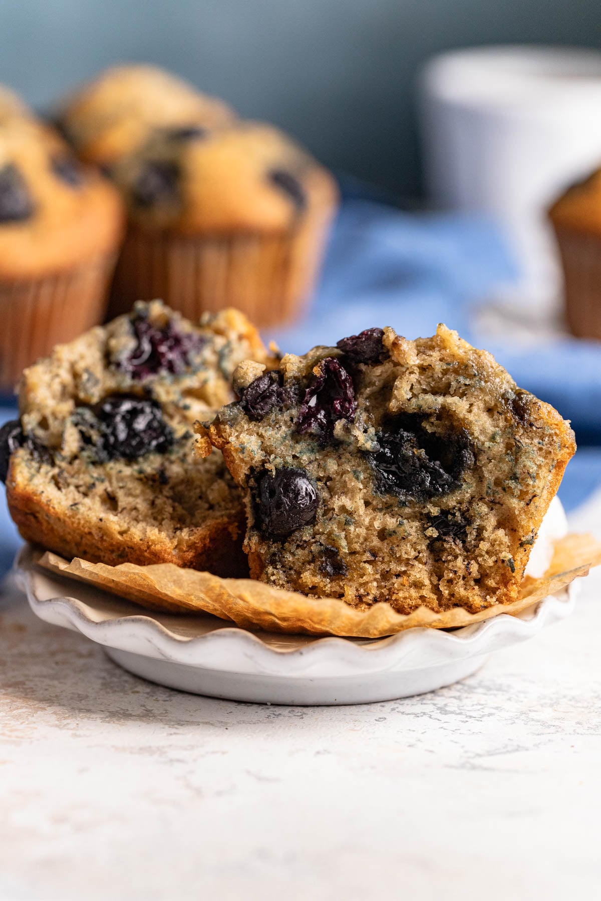 A blueberry banana muffin cut in half on a small plate.  There are purplish blue blueberries in each half
