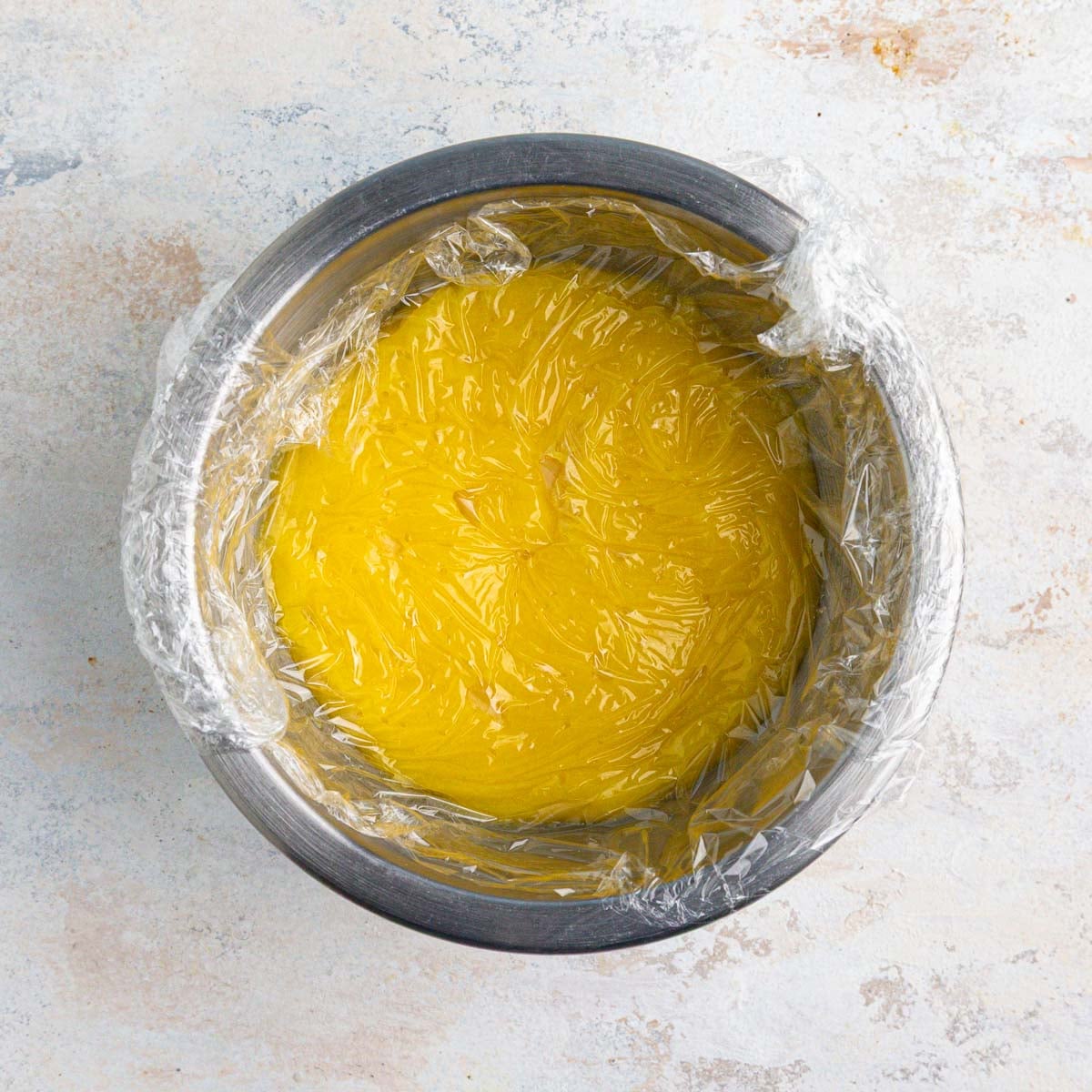 Lemon curd in a stainless steel bowl covered with plastic wrap