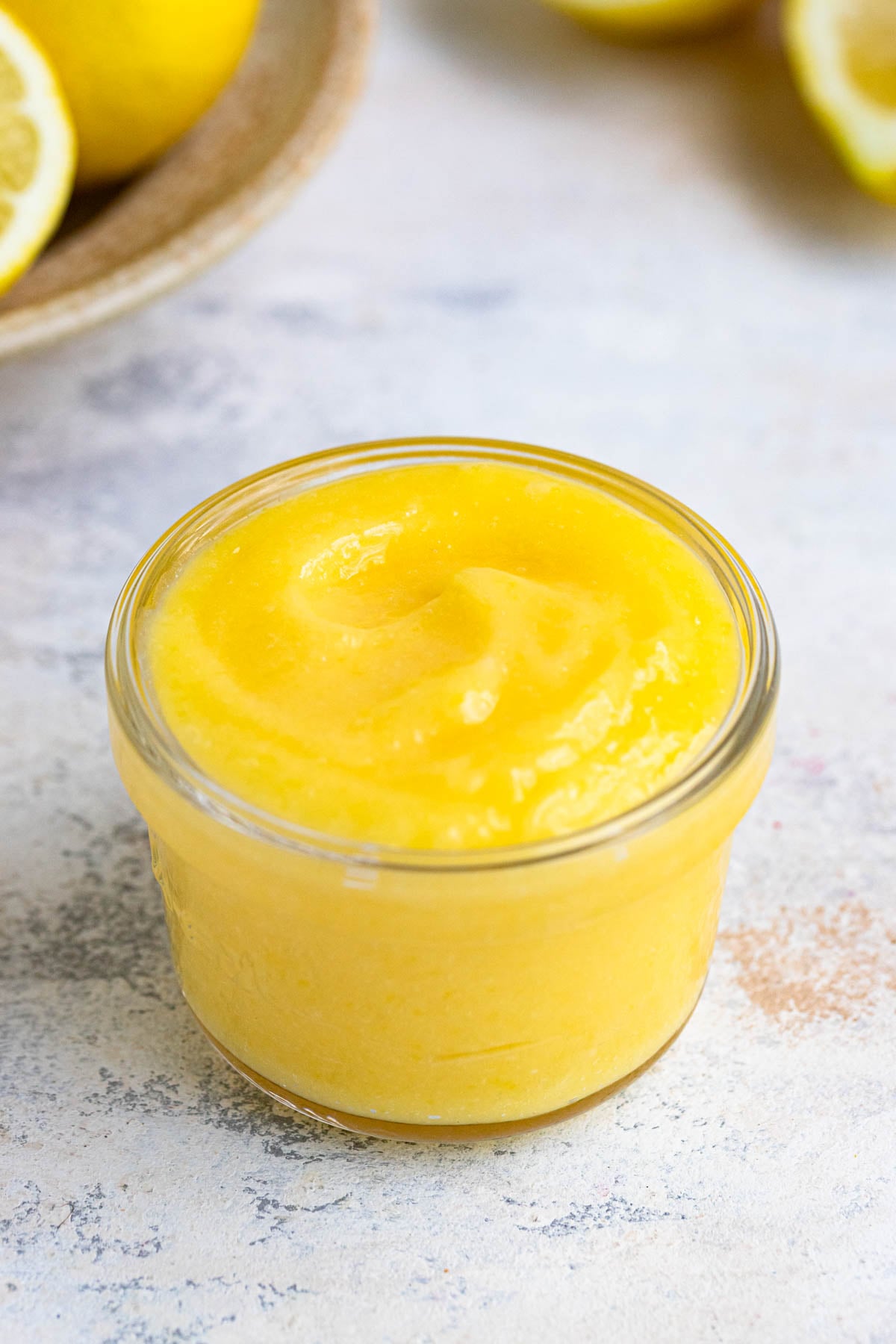 Lemon curd in a small class jar with fresh lemons in the background