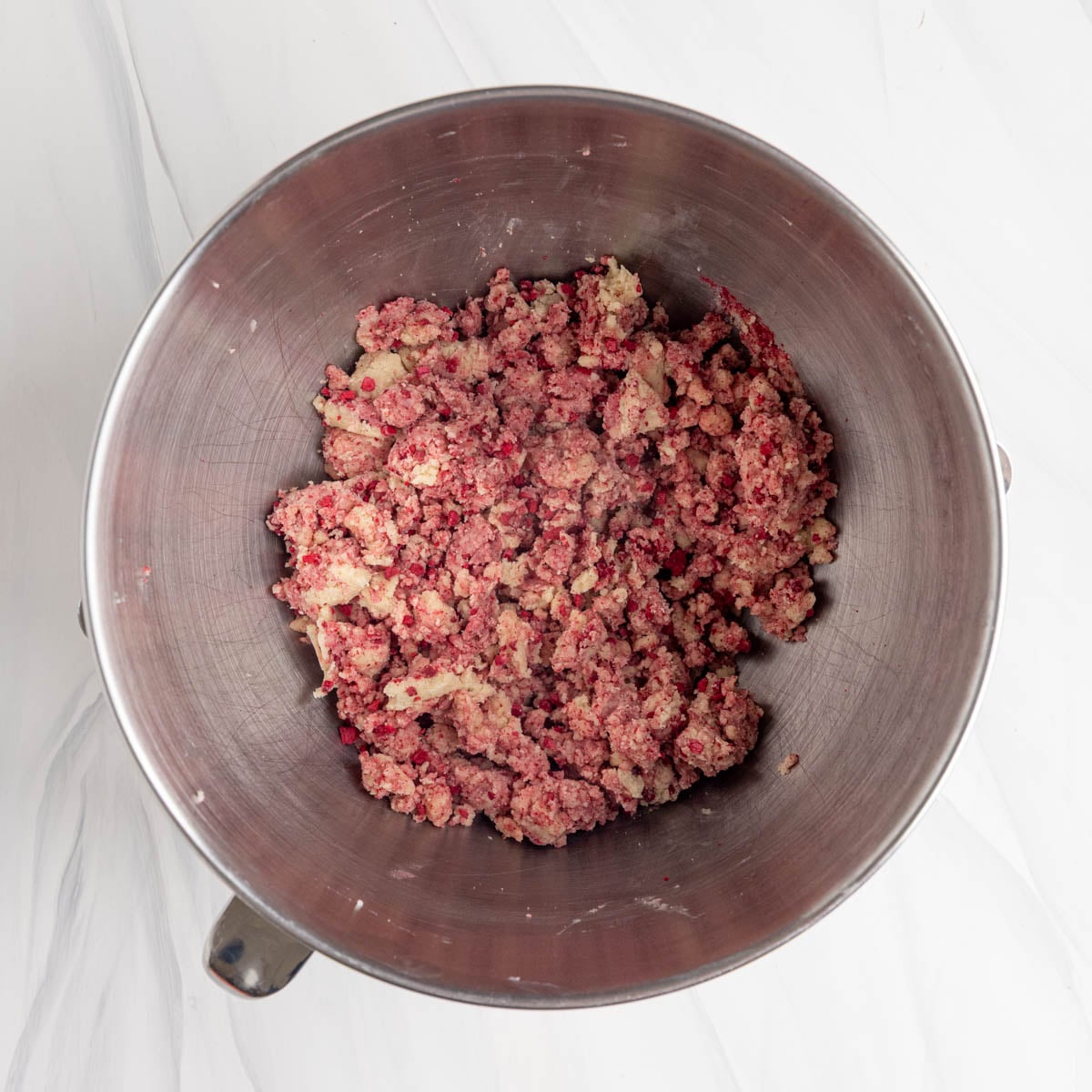 Raspberry shortbread cookie dough in the bowl of a stand mixer. The dough has a marbled appearance