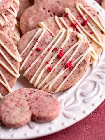 Raspberry shortbread cookies with a white chocolate drizzle arranged on a white ceramic plate