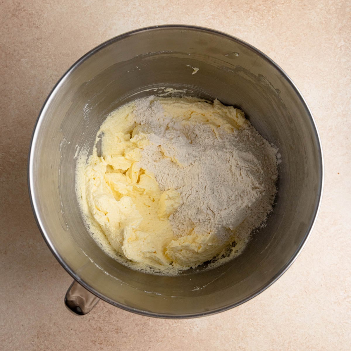 Cake batter in the bowl of a stand mixer with the dry ingredients sitting on top of the batter.