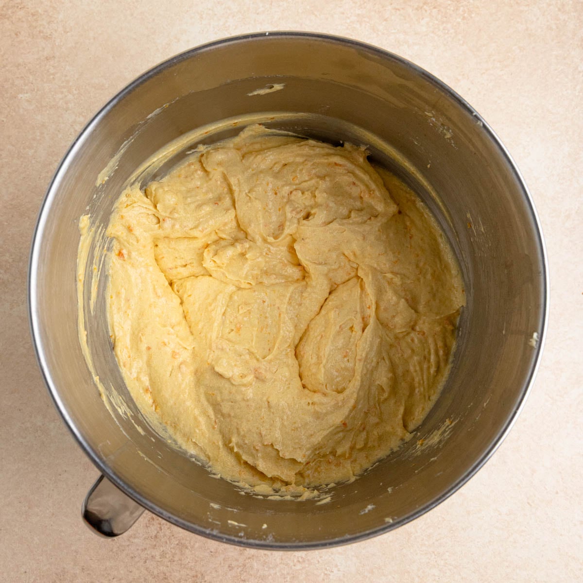 The clementine cake batter in the bowl of a stand mixer after all the ingredients are combined. The batter is orange and looks creamy