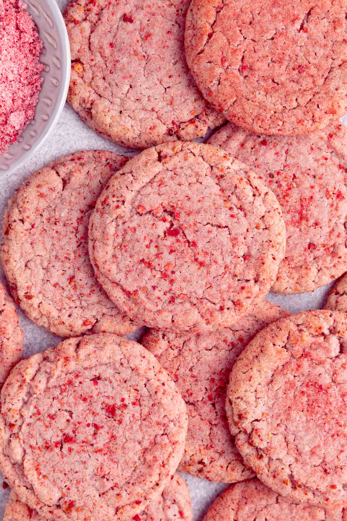 Several sugar cookies laid on a surface. The cookies are round, pink, with a strawberry sugar coating