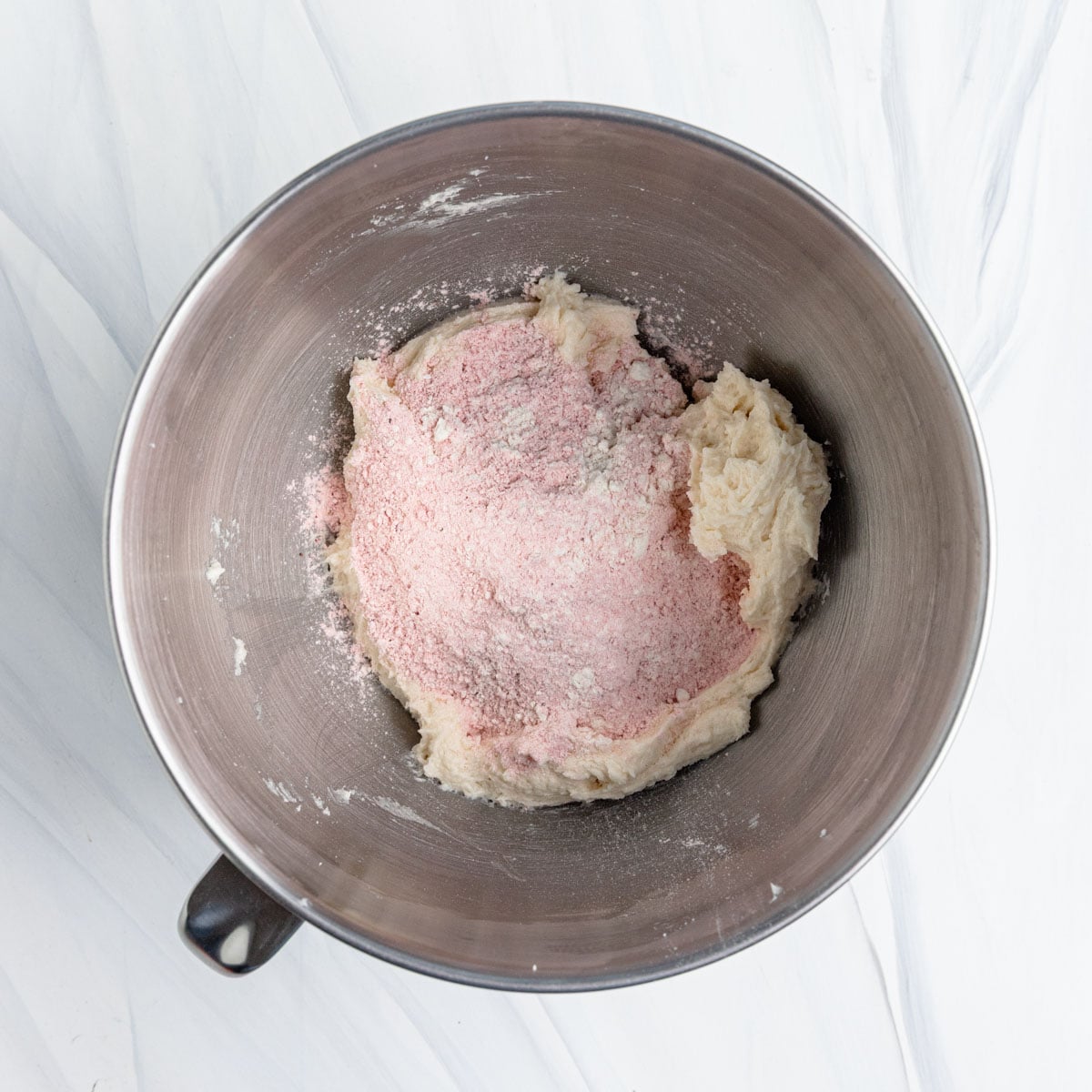 Strawberry flour mixture added to the cookie dough in a stainless steel bowl in a stand mixer