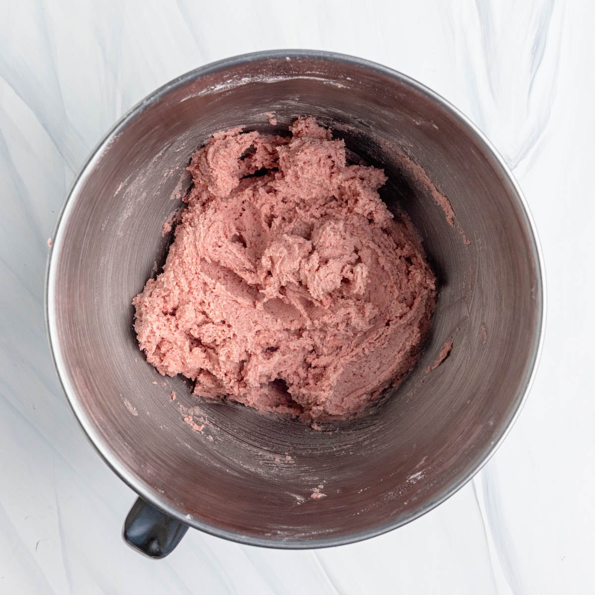Strawberry sugar cookie dough in a bowl of stand mixer. The dough is a bright pink color.