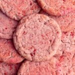 Several sugar cookies laid on a surface. The cookies are round, pink, with a strawberry sugar coating