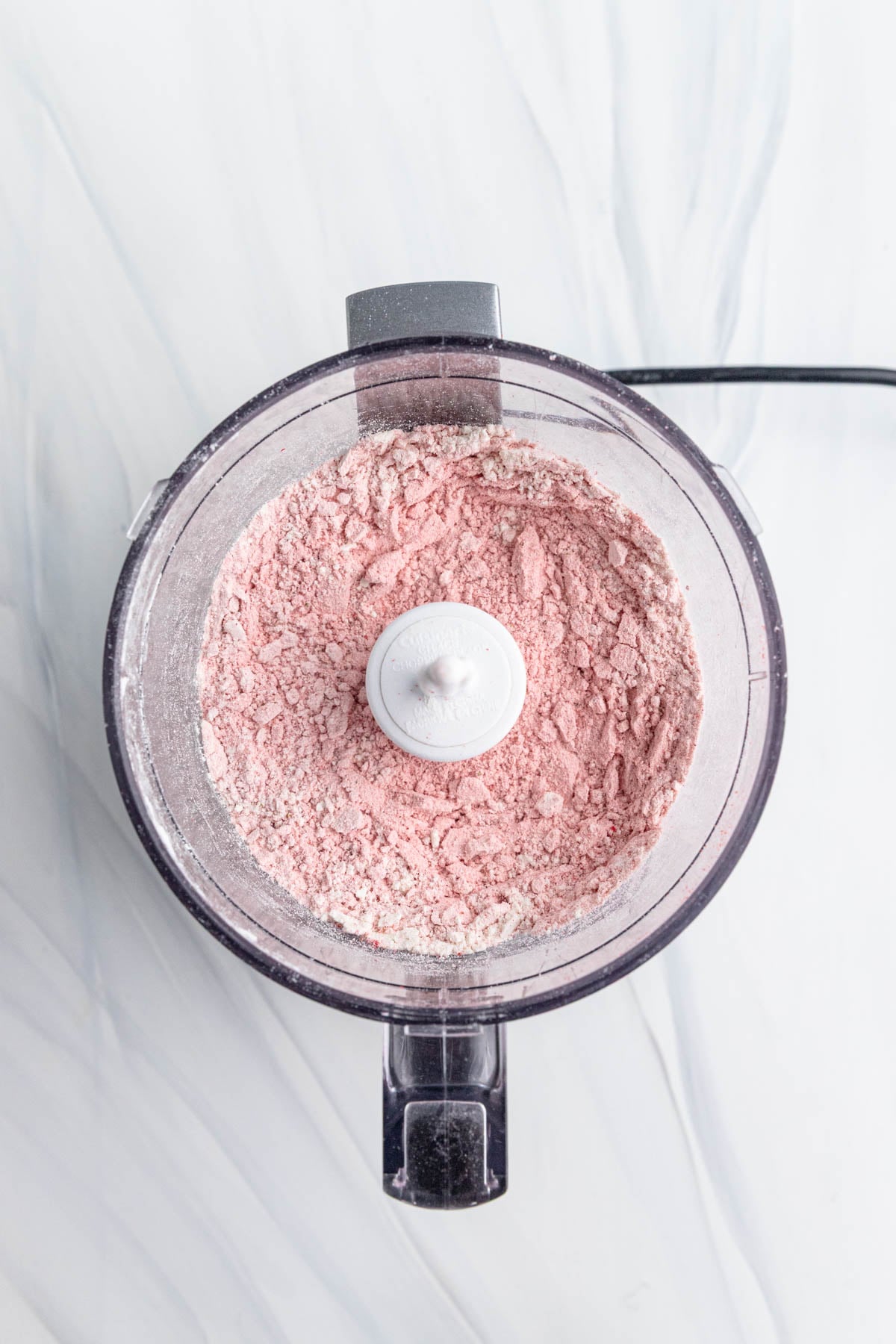 A combination of flour and pulverized freeze-dried strawberries in the bowl of a mini food processor.