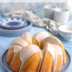 Vanilla Bundt Cake with a vanilla glaze on a blue plate with dessert plates and coffee cups in the background.