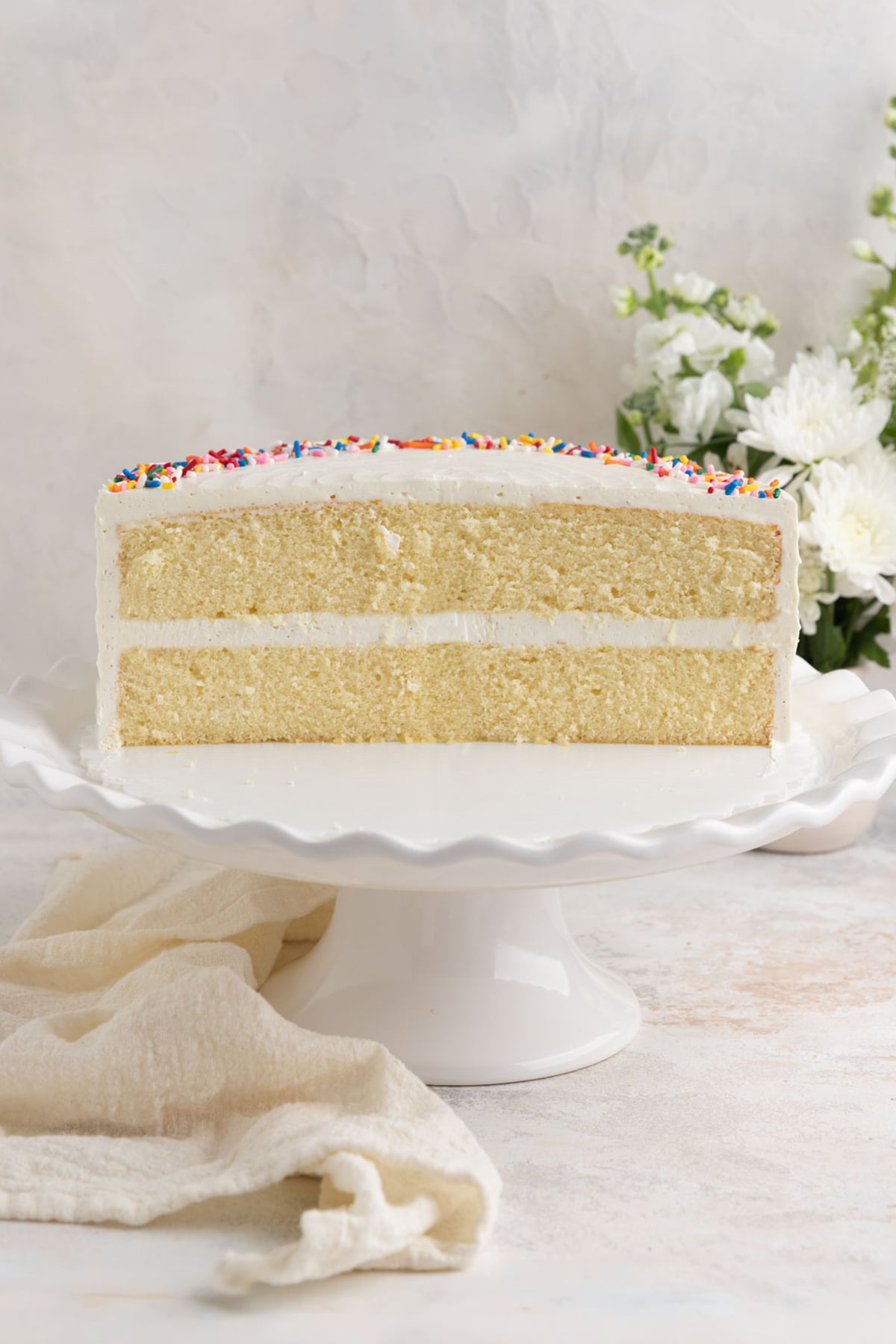 The vanilla cake cut in half. The cake crumb is fine and compact, and the frosting layers on the top, sides, and in the middle are visible