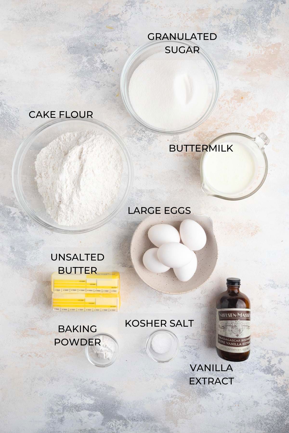 Vanilla Layer Cake ingredients arranged on a board - cake flour, granulated sugar, buttermilk, eggs, vanilla extract, kosher salt, baking powder, unsalted butter