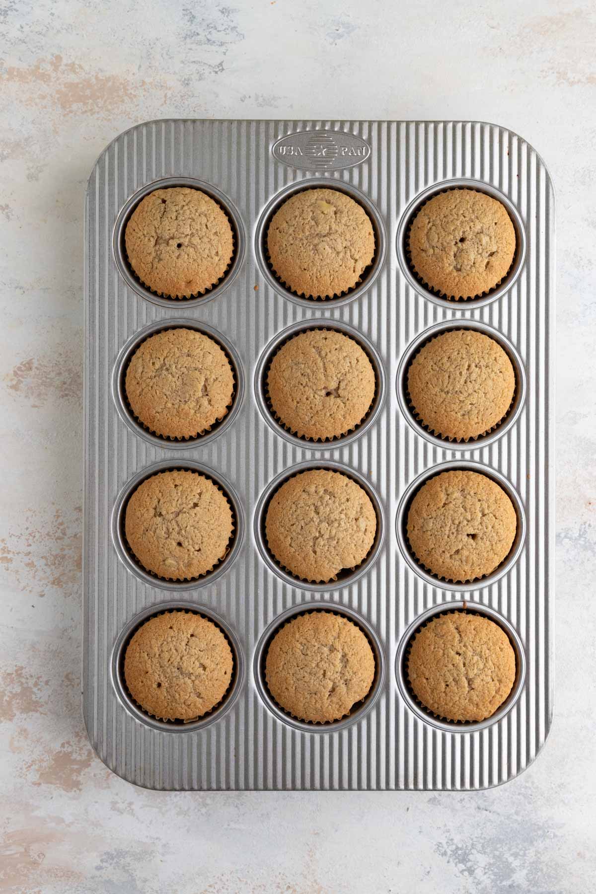 Baked banana cupcakes in a 12-cup muffin pan. The tops of the cupcakes are light brown and the tops are slightly craggly