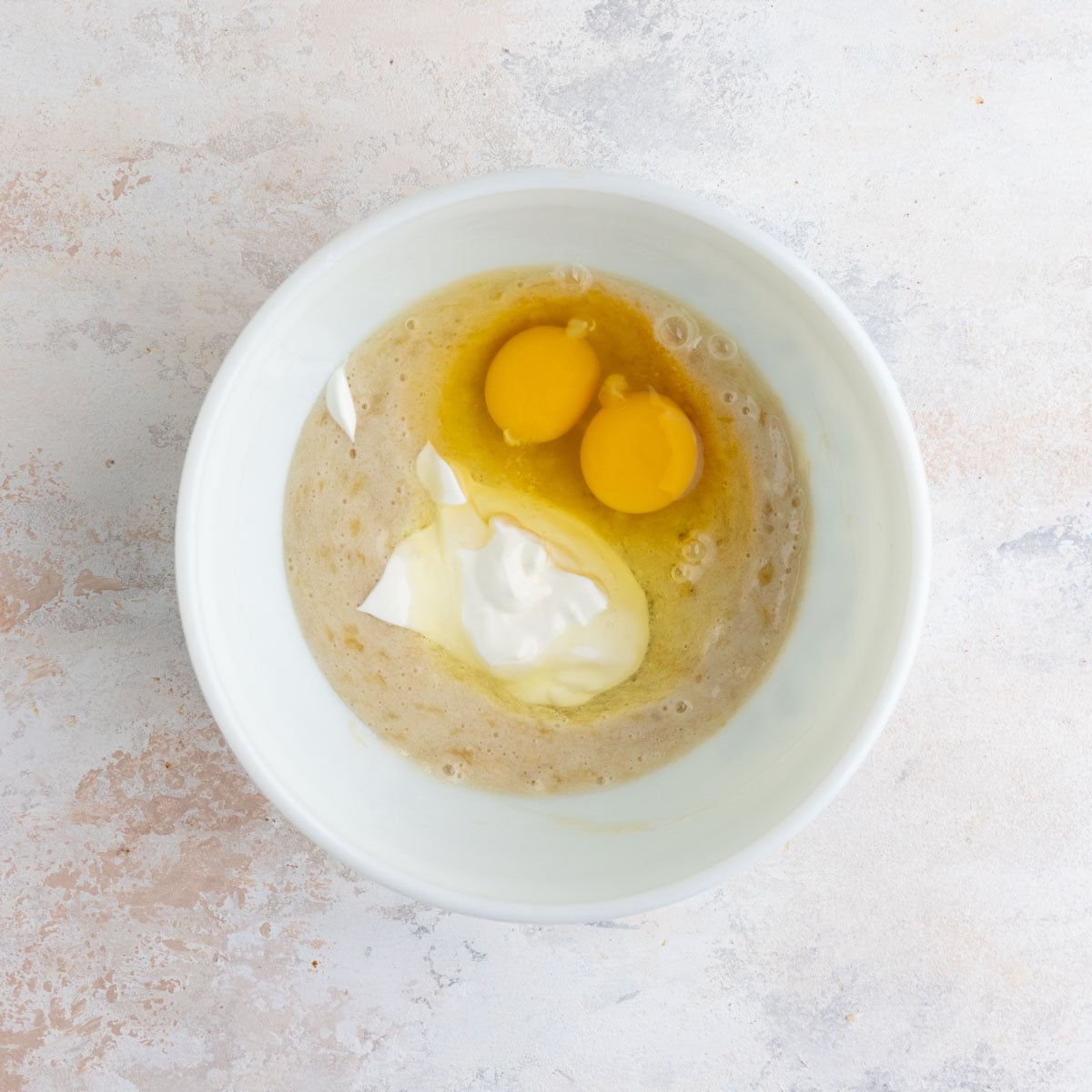 Pureed bananas in a white ceramic bowl with sour cream and two eggs.