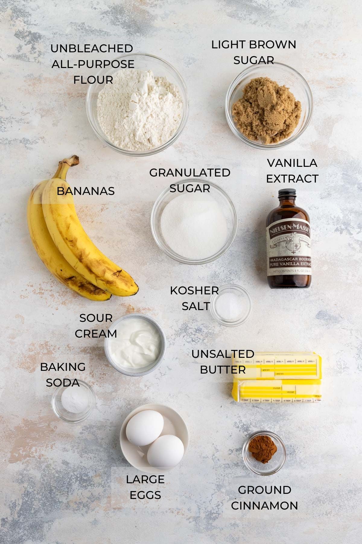 Banana Cupcake Ingredients (clockwise) - all-purpose flour, light brown sugar, pure vanilla extract, kosher salt, unsalted butter, ground cinnamon, large eggs, baking soda, sour cream, fresh bananas, granulated sugar