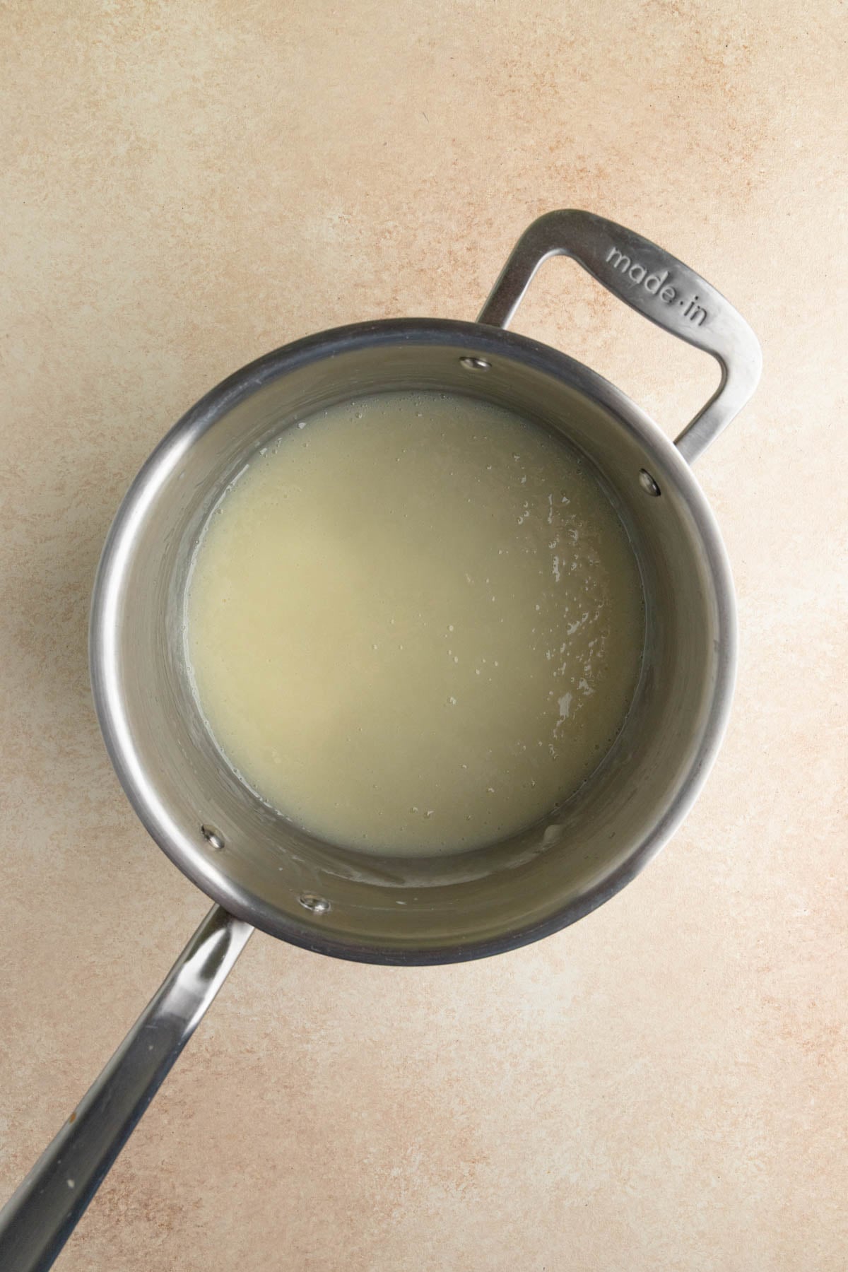 Cooked flour roux in a stainless steel saucepan.  The roux is shiny and has a slight yellow color.