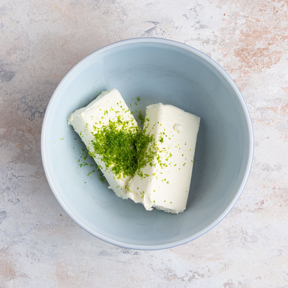 Key lime zest on top of 16 ounces of cream cheese in a ceramic mixing bowl