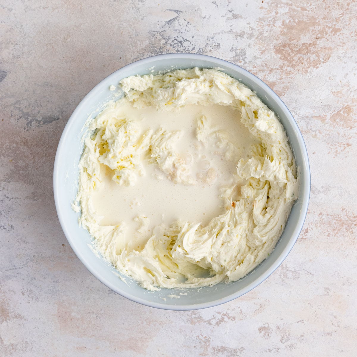 Heavy cream added to whipped cream cheese, mascarpone and sugar in a ceramic mixing bowl