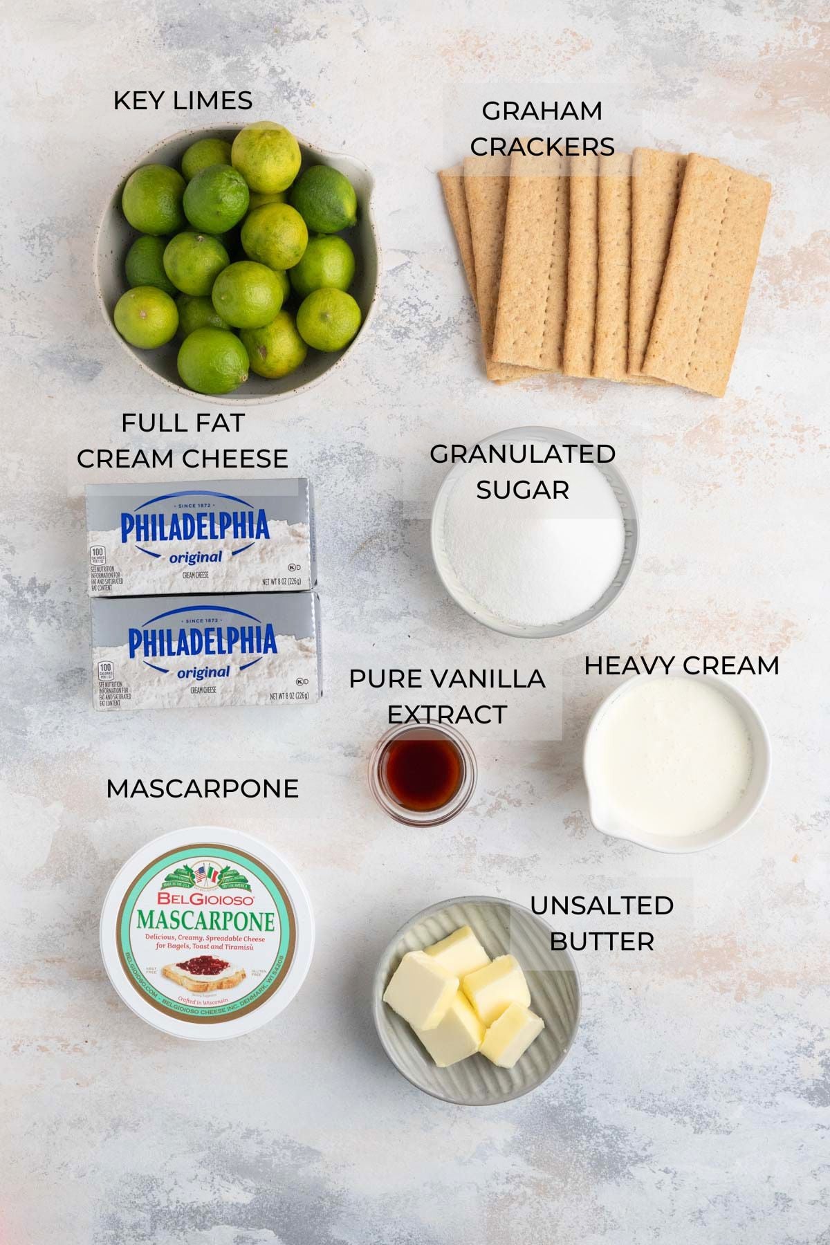 No bake key lime cheesecake ingredients clockwise: fresh key limes, graham crackers, granulated sugar, heavy cream, unsalted butter, vanilla extract, mascarpone cheese, cream cheese.