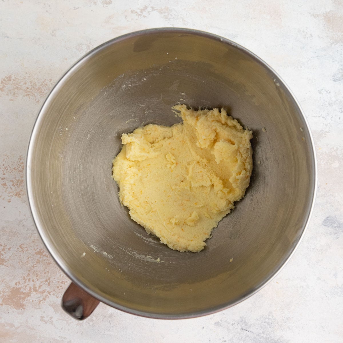 Creamed butter and sugar in a stainless steel mixing bowl. The mixture is a light orange from the orange zest.