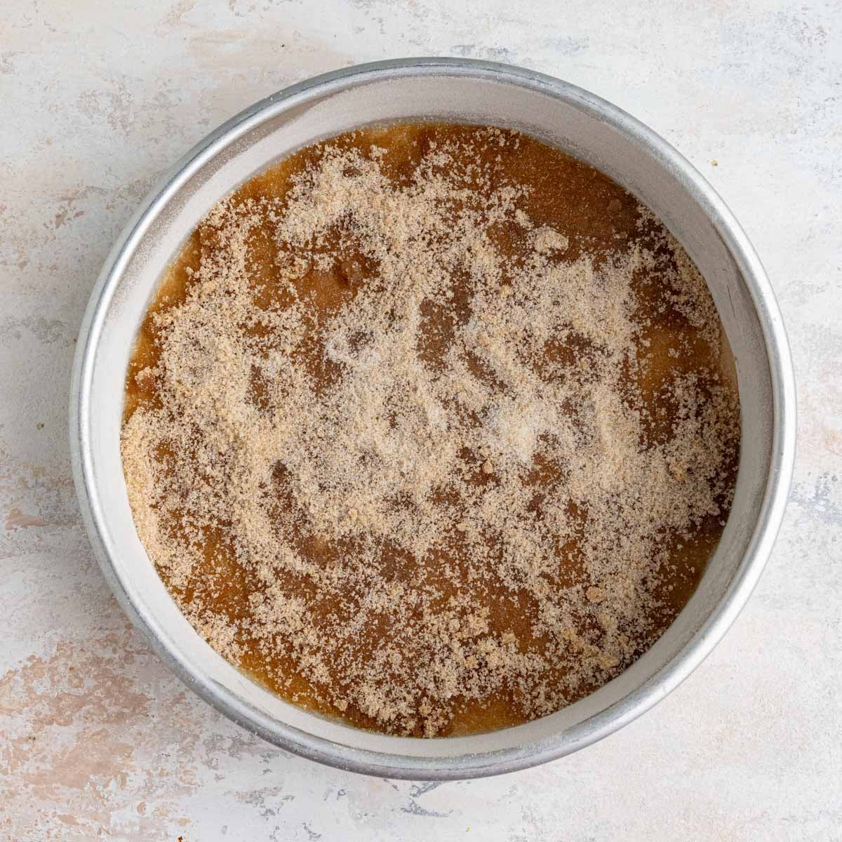 The 9x2-inch round cake pan with a layer of white and brown sugar on top of the melted butter.
