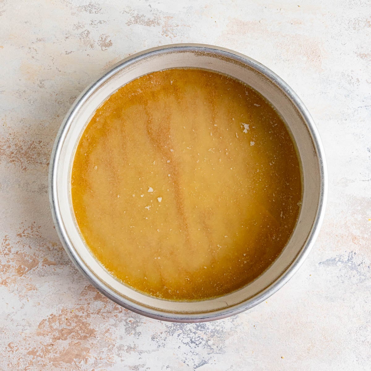 9x2-inch round cake pan lined with a piece of brown parchment paper. There is melted butter on top of the parchment paper.