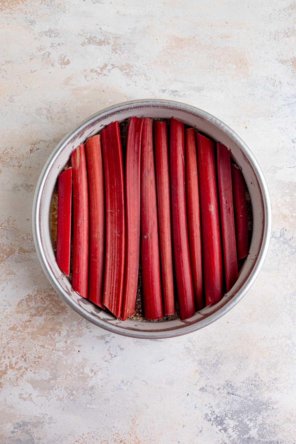 The 9x2-inch round cake pan filled with red stalks of fresh rhubarb.