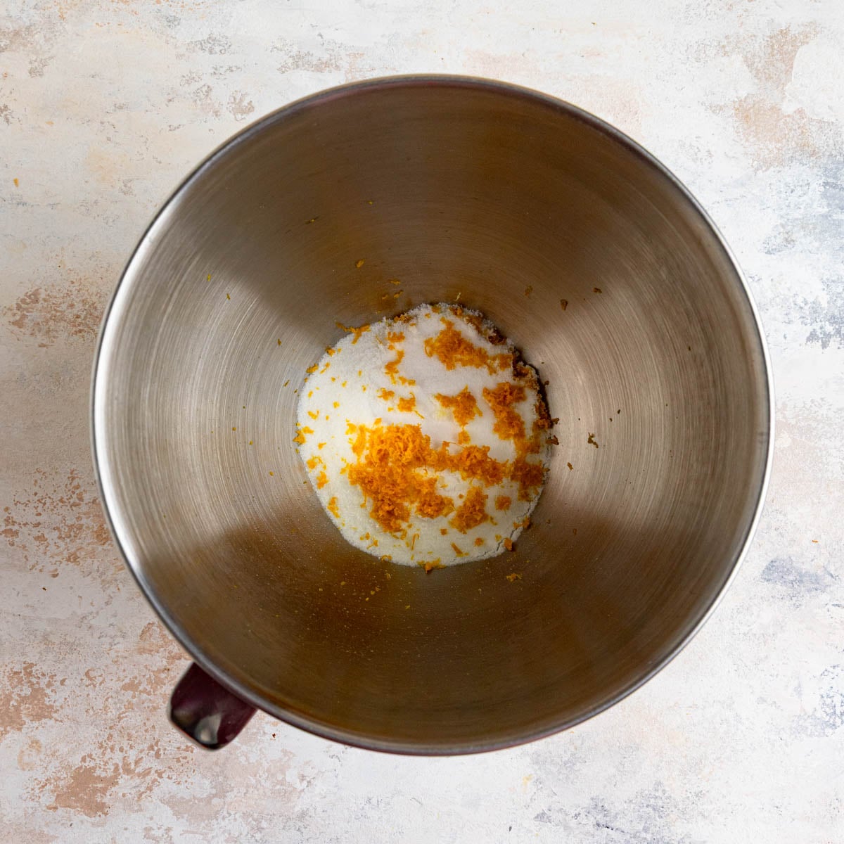 A stainless steel mixing bowl filled with granulated sugar and orange zest