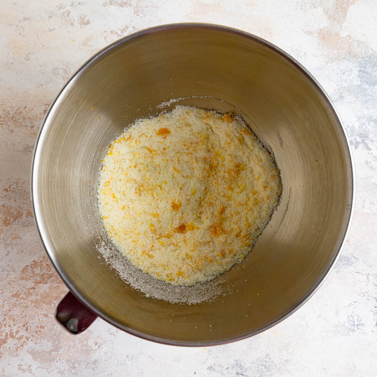 Stainless steel mixing bowl filled with orange zest rubbed into granulated sugar. The sugar looks orange.