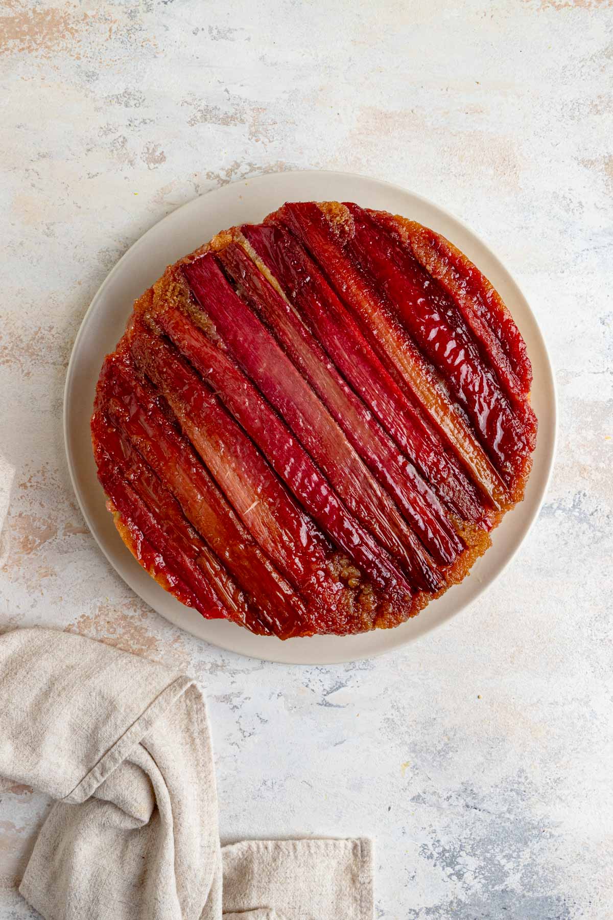 The rhubarb upside down cake inverted onto a white plate. The top of the cake pieces of rhubarb across the top.