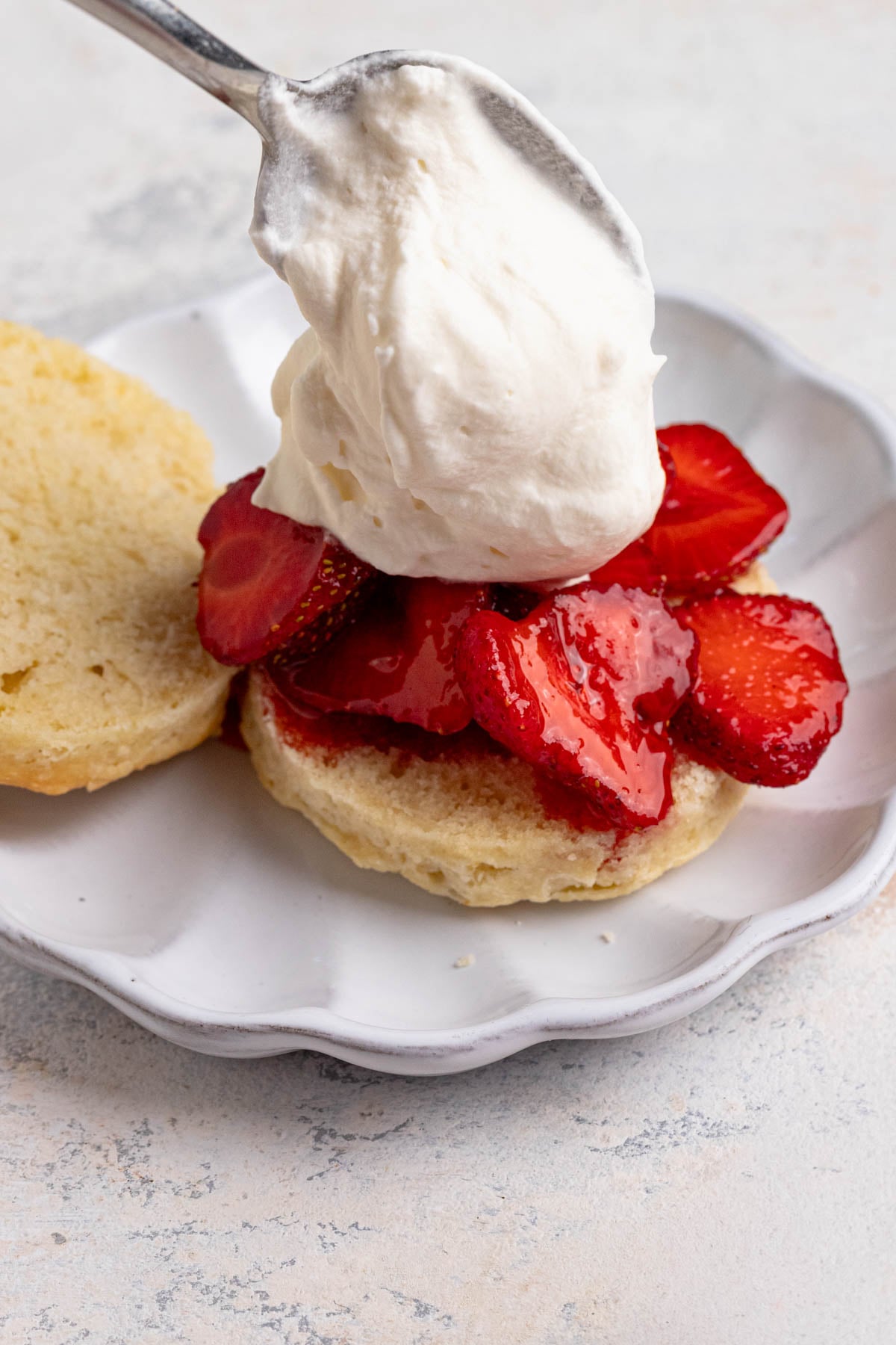 Whipped cream being spooned over fresh strawberries on top of a sweet shortcake biscuit