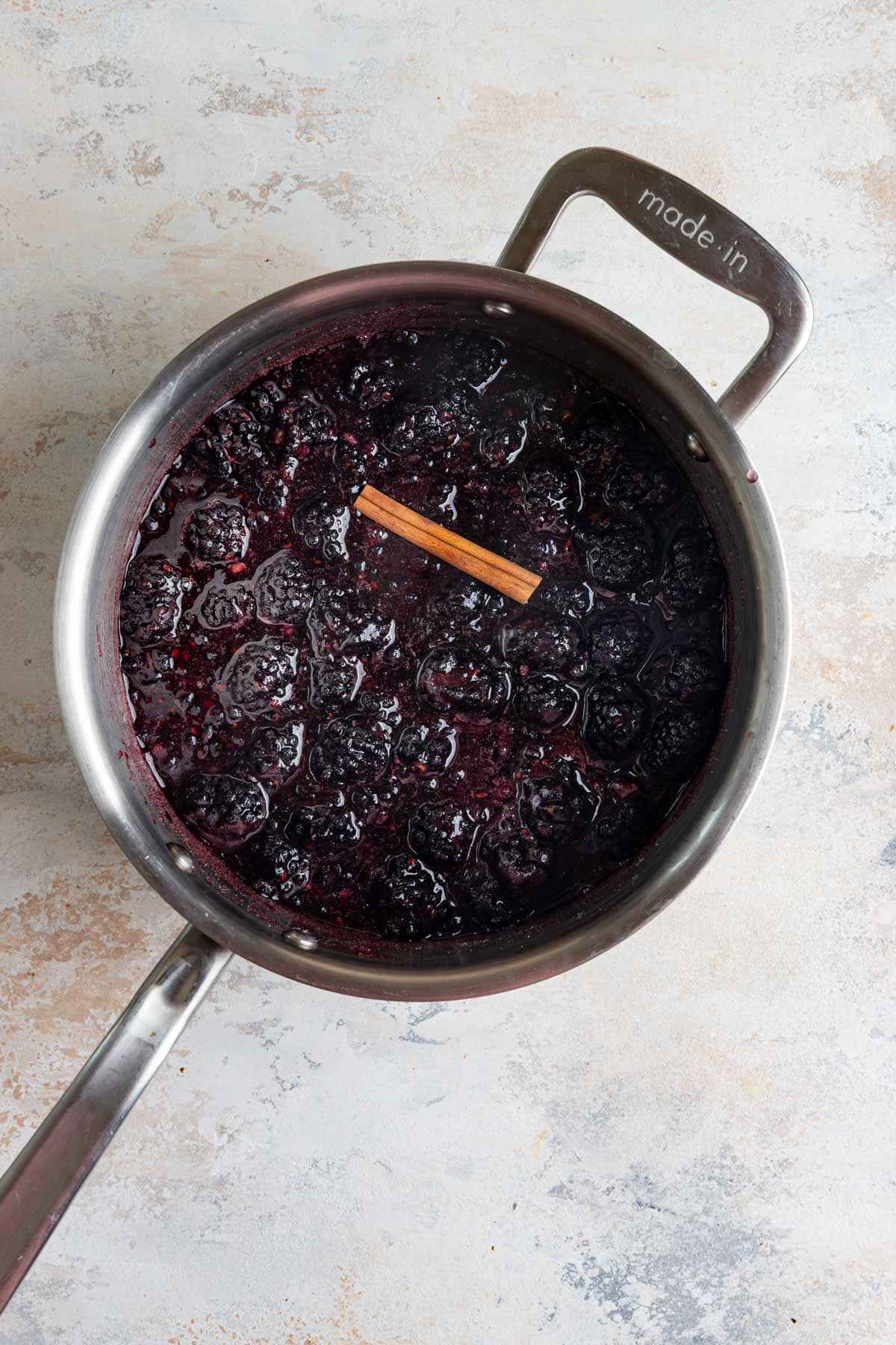 Fresh blackberries, lemon juice, sugar, and a cinnamon stick in a stainless steel pot