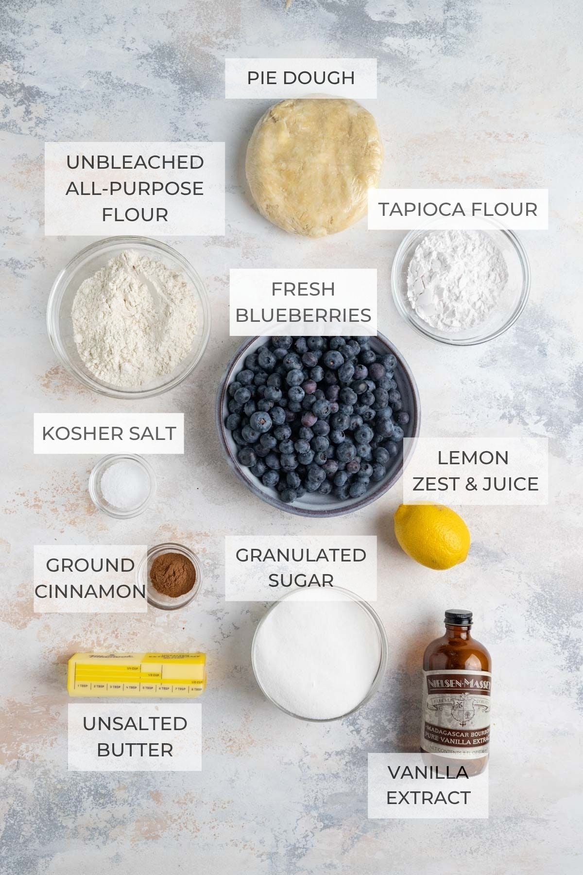Blueberry crumble pie ingredients clockwise: pie dough, tapioca flour, fresh blueberries, a lemon, vanilla extract, granulated sugar, ground cinnamon, kosher salt, unbleached all-purpose flour
