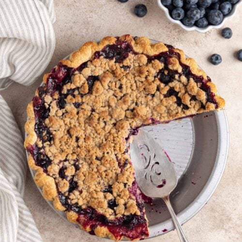 Blueberry crumble pie with two slices cut out. A pie server in the pie plate.
