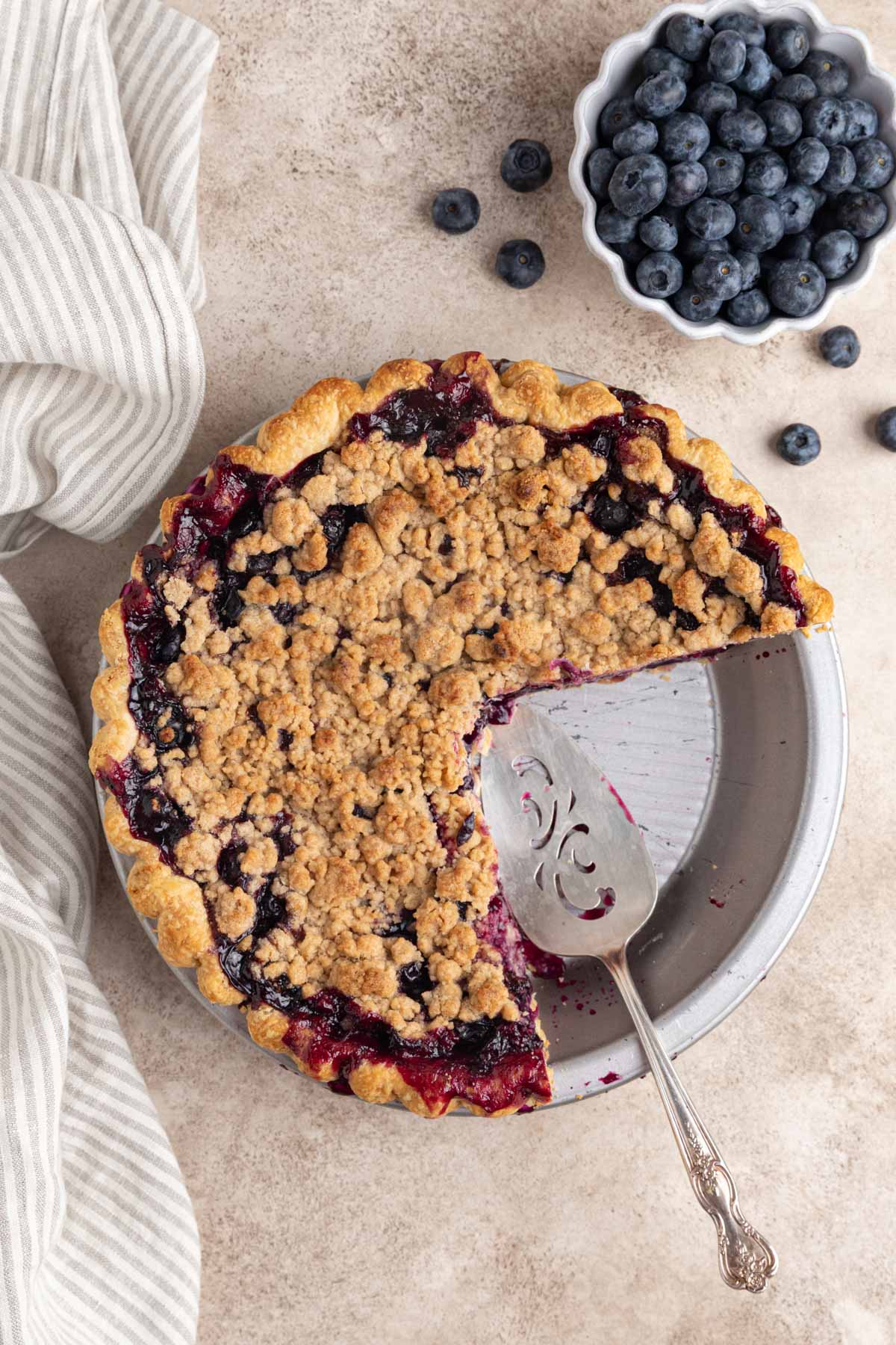 Blueberry crumble pie with two slices cut out. A pie server in the pie plate.