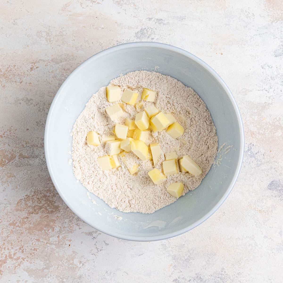 Flour, salt, cinnamon and cubed butter in a white ceramic bowl.