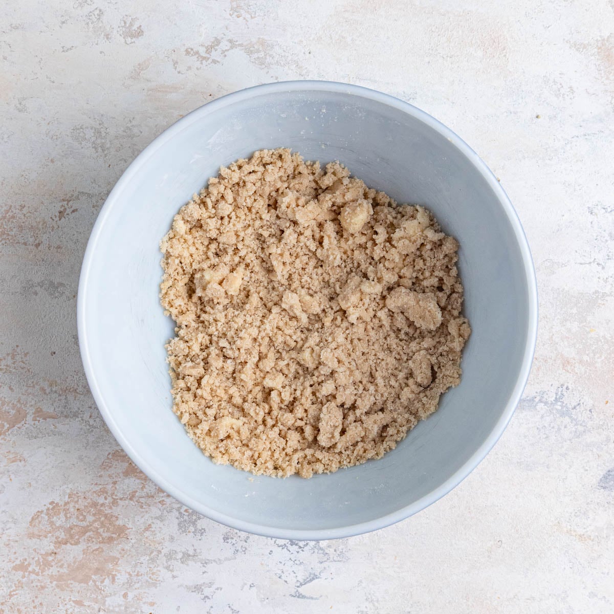 The prepared crumble in a large ceramic bowl. The crumble is a light brown color.