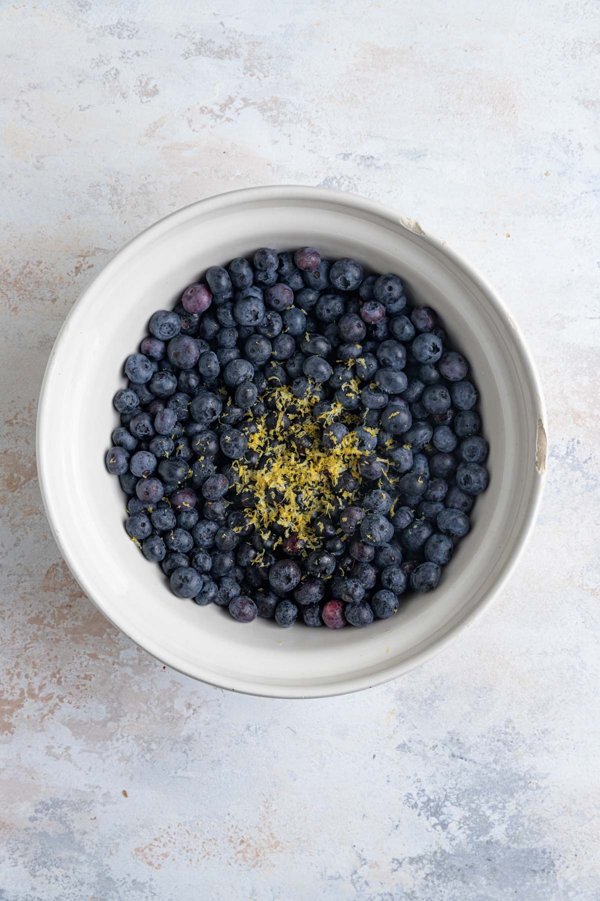 Blueberries in a large ceramic bowl with lemon zest on top of the blueberries