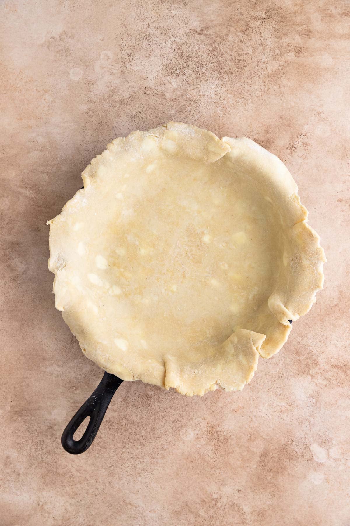 Pie dough rolled out and placed inside a cast-iron pan. The dough is hanging over the edges of the pan